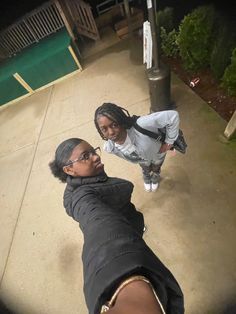 two women taking a selfie in front of a sign post at night, one woman is wearing glasses and the other has her hand on her hip