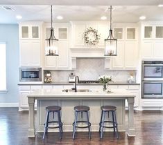 an open kitchen and living room with hardwood floors, white cabinets and bar stools