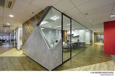 an office with glass walls and wooden flooring on the inside wall is a triangular shaped cubicle