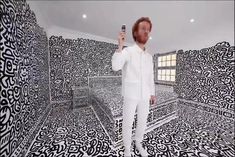 a man holding a cell phone in front of a room with black and white designs