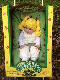 a baby doll in a green and yellow box sitting on the grass with its head turned to look like she's wearing a hat