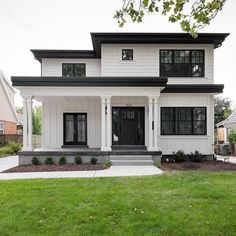 a white two story house with black trim on the front door and windows, grass in front of it