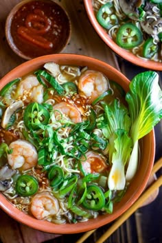 two bowls filled with soup and vegetables on top of a wooden table next to chopsticks