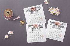 two calendar cards sitting on top of a table next to flowers and a tape measure