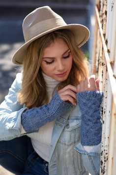 a woman leaning against a rail wearing a hat and blue jeans with her hands on the rails