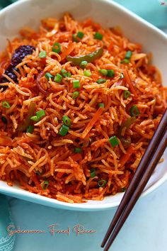 a bowl filled with carrots and green onions next to chopsticks on a table