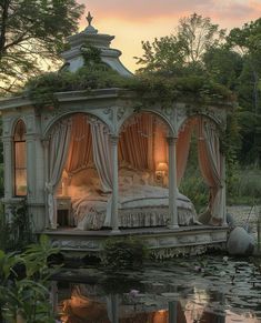 a bed sitting on top of a lush green field next to a lake at sunset