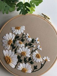 white daisies are embroidered onto a beige hoop