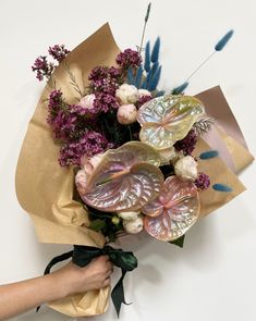 a person holding a bouquet of flowers on top of a white table next to a brown paper bag