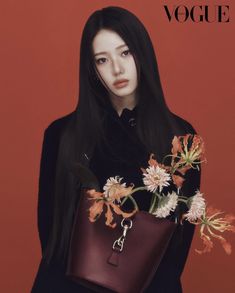 a woman with long black hair holding a brown bag and flowers in front of her face