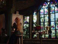 a woman sitting at a table in front of stained glass windows with flowers on it