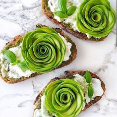 three pieces of bread with cream cheese and green leaves on them, sitting on a marble surface