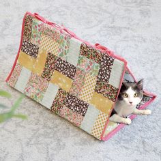 a cat sitting inside of a patchwork purse on the floor next to a plant