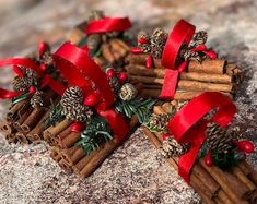 cinnamon sticks wrapped in red ribbon with pine cones and berries on them sitting on top of a rock