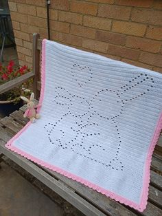 a white crocheted blanket with pink trim sitting on a wooden bench next to a potted plant