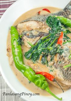 a white plate topped with fish covered in gravy and green chili peppers on top of it