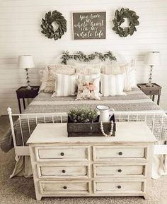 a white bed sitting in a bedroom next to a dresser and table with flowers on it