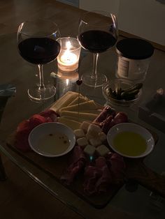 two glasses of wine are sitting on a table with meat and cheese in front of them