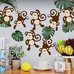 three monkeys hanging from the ceiling above a table with fruit and coffee cups on it