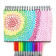 a notebook with markers and pens on top of it, in front of a white background