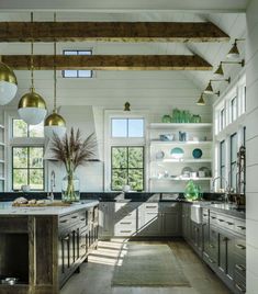 an open kitchen with lots of counter space and hanging lights above the island area, along with large windows