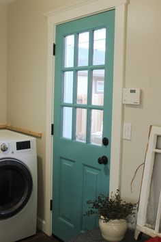 a washer and dryer sitting in front of a door with a potted plant next to it