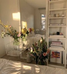 two vases filled with flowers sitting on top of a bed next to a book shelf