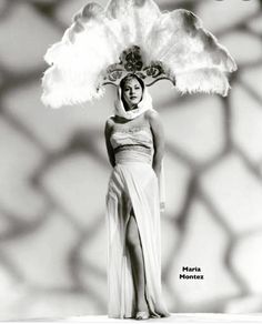 a woman in a long white dress and large feathered headdress poses for a photo