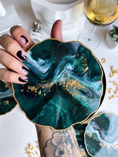 a woman's hand with black and gold nails holding a green marble bowl on top of a table