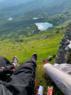 two people laying on the ground with their feet up in the air, overlooking mountains and lakes