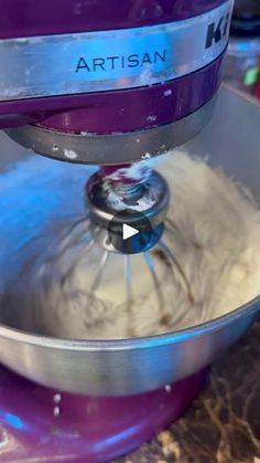 an artisan mixer mixing white batter in a purple bowl with the words artisan on it