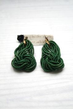 green earrings with black beads and gold accents on a white cloth covered surface, close - up