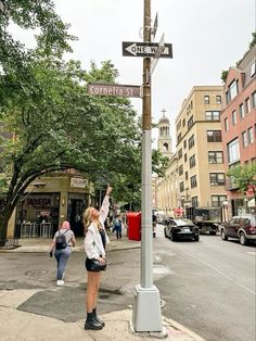 a woman points at a street sign on a pole in the middle of a city