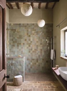 a bathroom with two round lights hanging from the ceiling and a tiled shower area in front of it