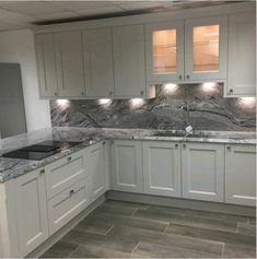 an empty kitchen with marble counter tops and white cupboards on the wall, along with gray tile flooring