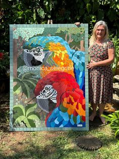 a woman standing next to a colorful parrot art piece on display in front of trees