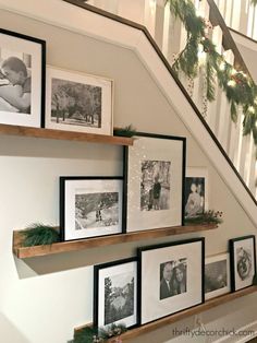 some pictures are hanging on the wall near stairs and christmas garlands in front of them