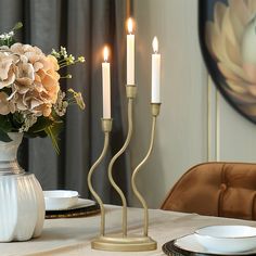 three candles are lit on a table with plates and flowers