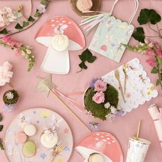 a pink table topped with plates and cups filled with desserts next to greenery