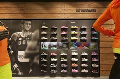 two women standing in front of a display of running shoes on the side of a wall