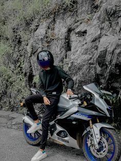 a man sitting on the back of a motorcycle next to a rock wall and grass