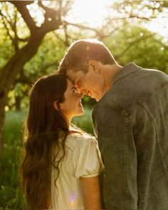 a young man and woman standing next to each other in the grass with trees behind them