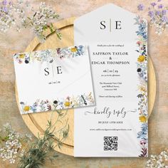 the wedding stationery is laid out on a wooden plate with flowers and greenery