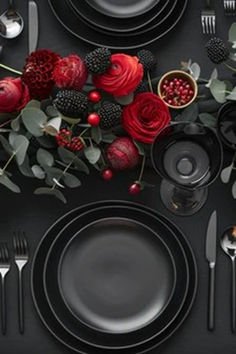 the table is set with black plates, silverware and red rose centerpieces