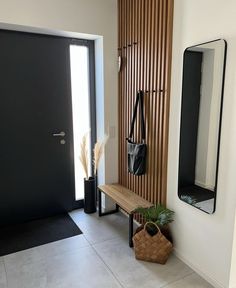 a wooden bench sitting in front of a black door next to a mirror and potted plant