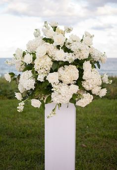 a white vase filled with flowers on top of a lush green field next to the ocean