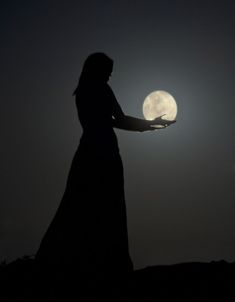 the silhouette of a woman holding out her hand at night with the moon in the background