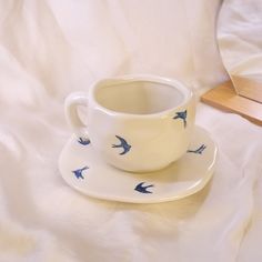 a white cup and saucer with blue birds on it sitting on a white bed