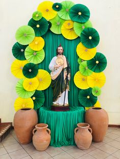 a statue of jesus surrounded by green and yellow paper umbrellas in front of a wall