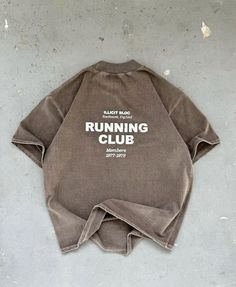 a brown running club shirt sitting on top of a cement floor with the words running club printed on it